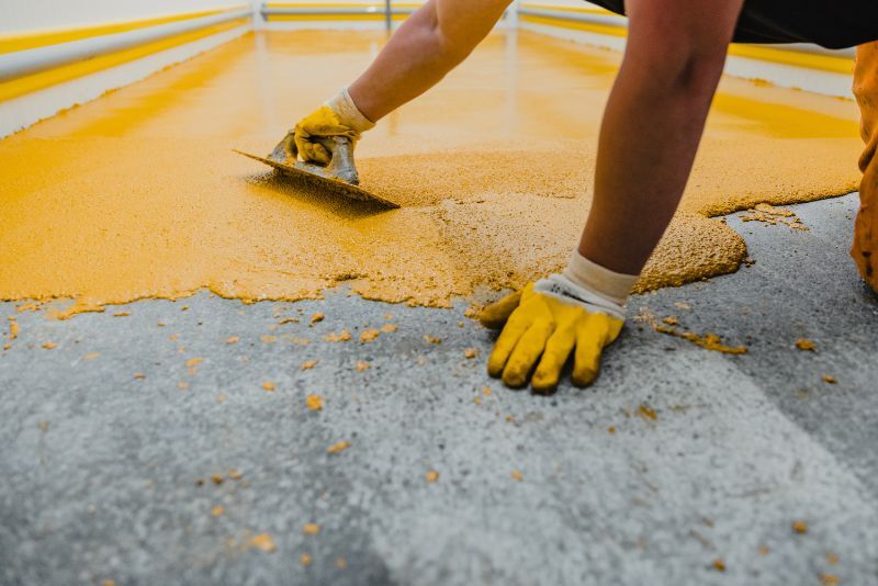 Tradesperson trowelling bright yellow epoxy coating onto a concrete floor